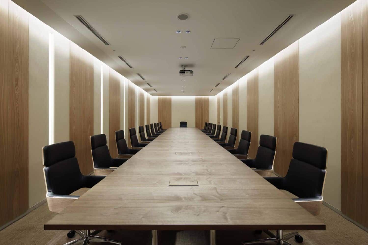 Moderner Konferenzraum mit langem Holztisch und ergonomischen Stühlen unter dezenter Beleuchtung.