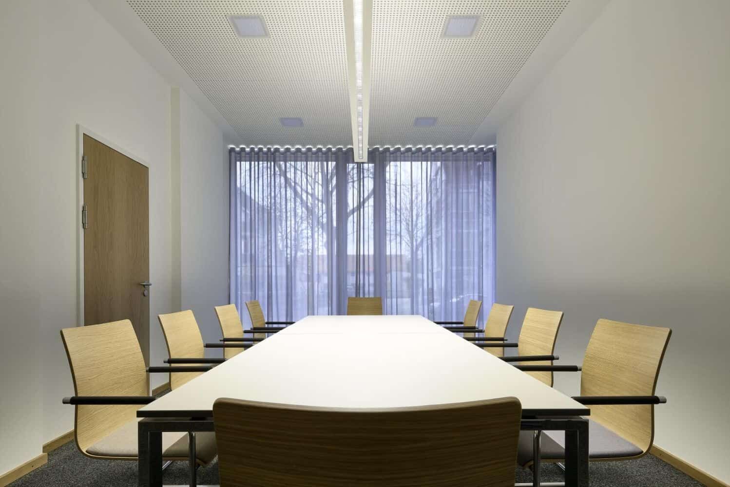 Moderner Konferenzraum mit großem Tisch, umgeben von ergonomischen, hölzernen Bürostühlen und natürlichem Licht.