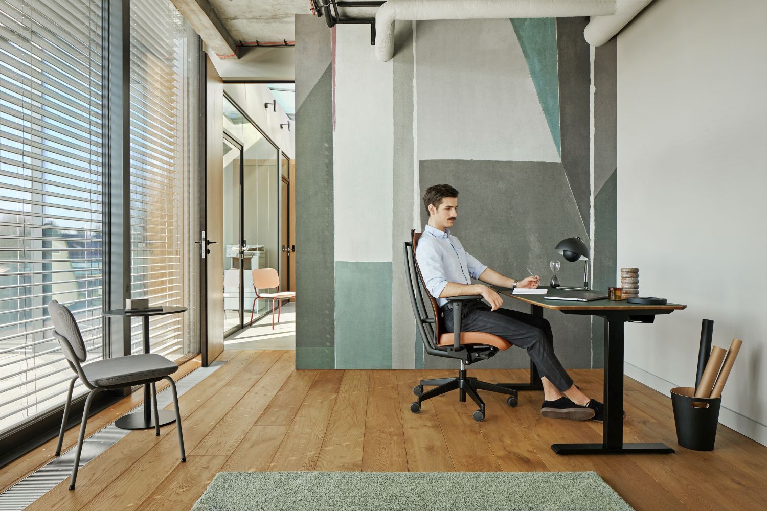 Mann sitzt in ergonomischem Bürostuhl an modernem Schreibtisch in stilvollem, gut beleuchtetem Raum mit Holzboden.