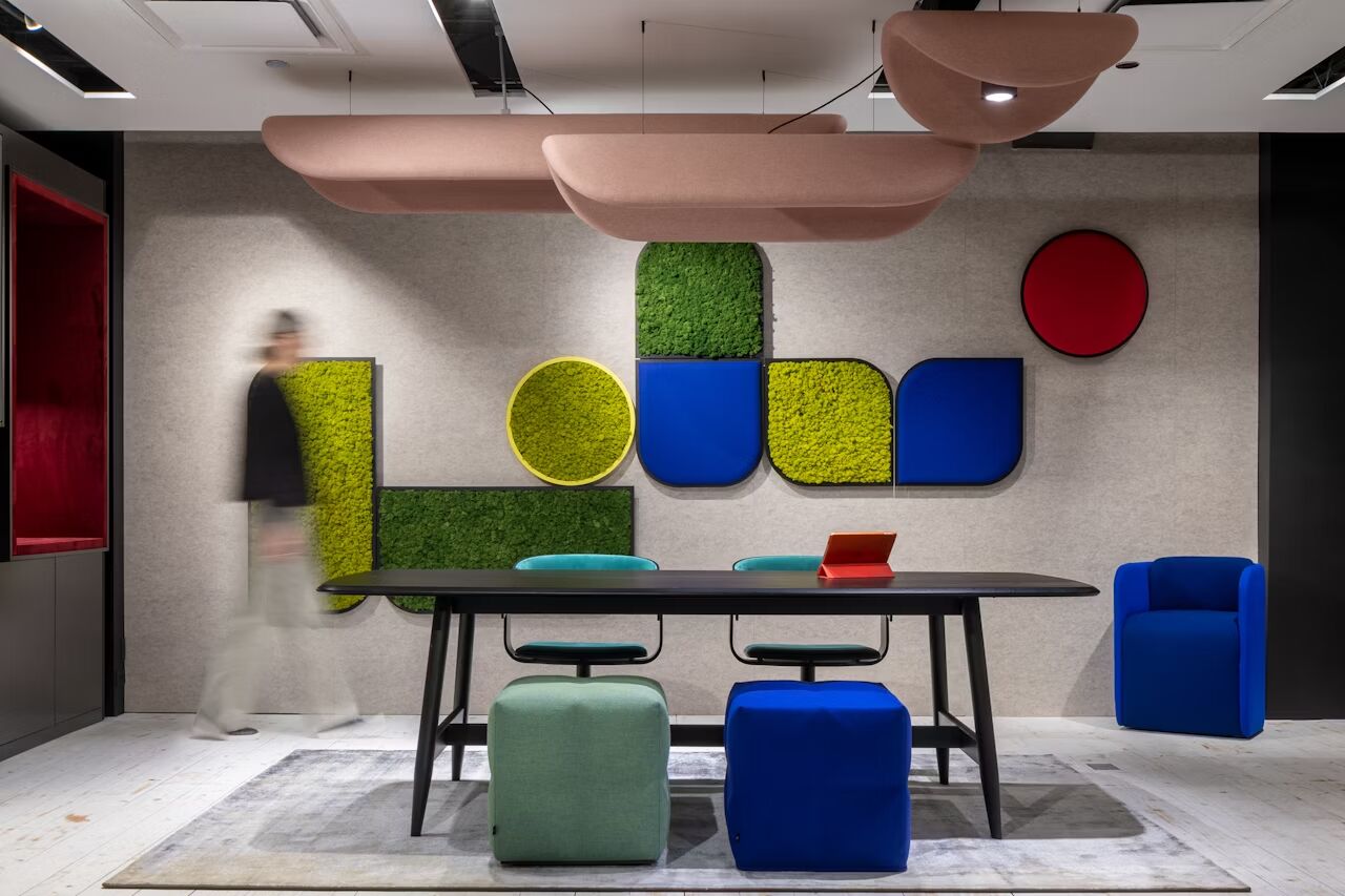 Modernes Büro mit farbenfroher Wanddekoration, Tisch, Stühlen und einer Person, die vorbeigeht.
