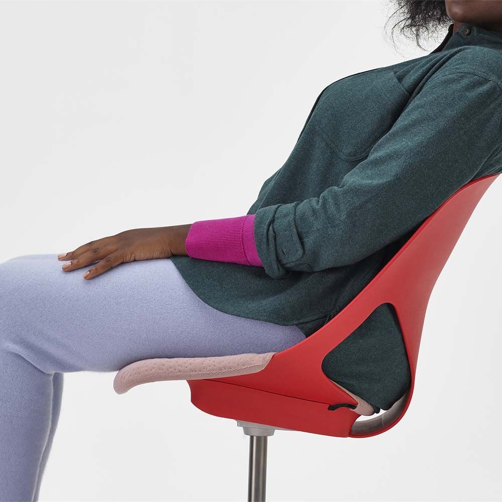 Person sitzt ergonomisch auf einem roten Stuhl, betont dynamisches Sitzen und gute Haltung.