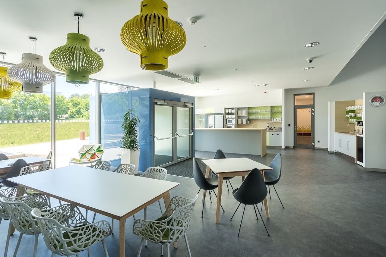 Modernes Büro-Küchen- und Lounge-Bereich mit stilvollen Möbeln und großen Fenstern, die viel natürliches Licht hereinlassen.