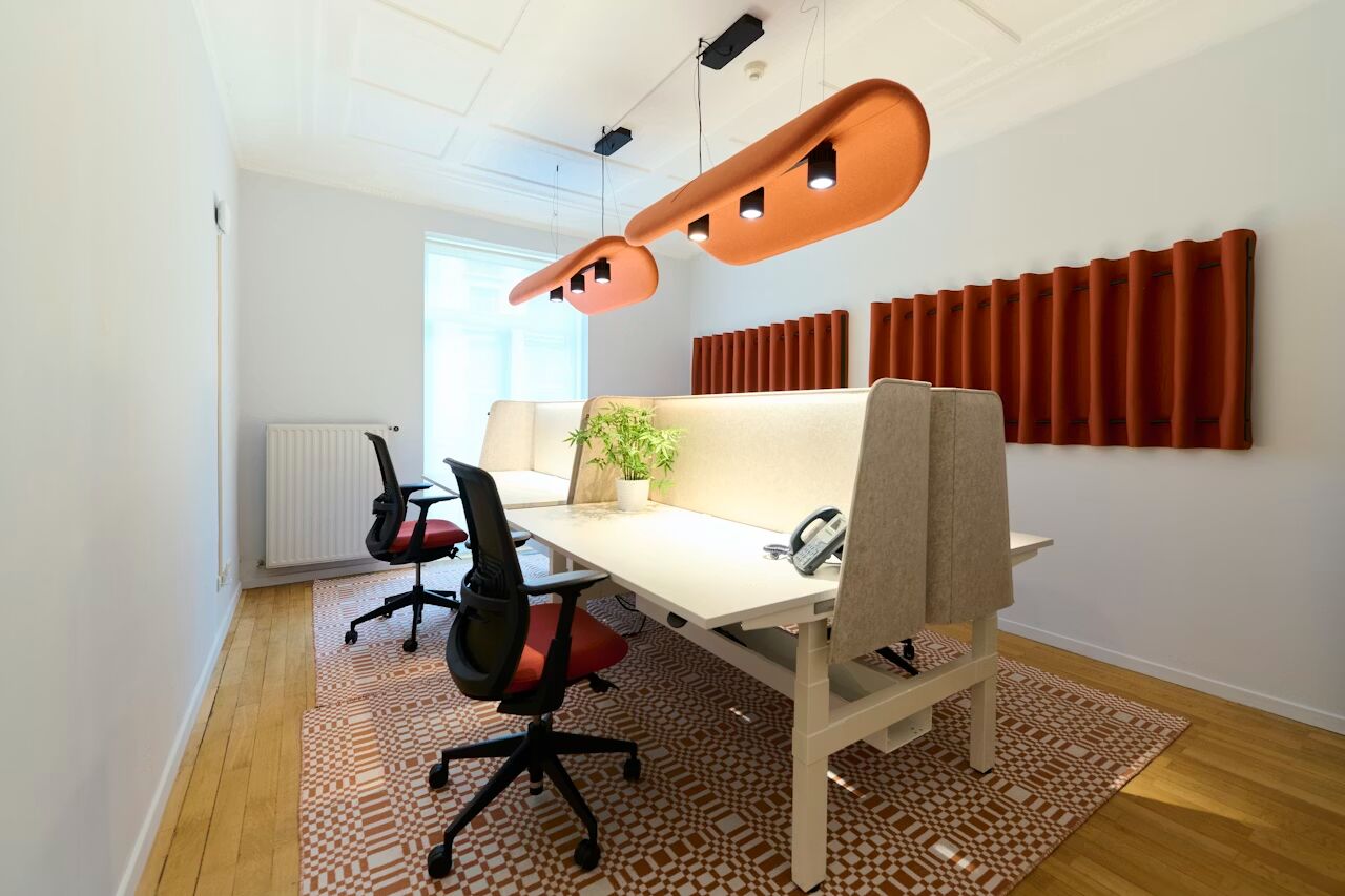 Modernes Büro mit ergonomischen Bürostühlen, weißen Tischen, Pflanzen und orangefarbenen Akustikpaneelen an den Wänden.