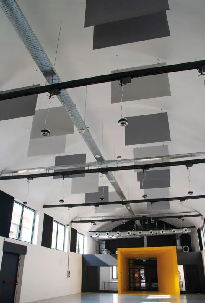 Moderne Industriehalle mit hohen Decken und gelbem Eingang, ausgestattet mit Schallschutzplatten und Lüftungsrohren.