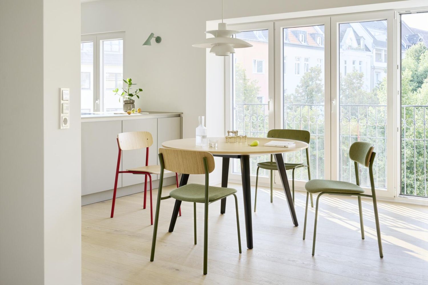 Moderne Esszimmer-Einrichtung mit rundem Tisch und vier Stühlen in einem lichtdurchfluteten Raum mit großen Fenstern.