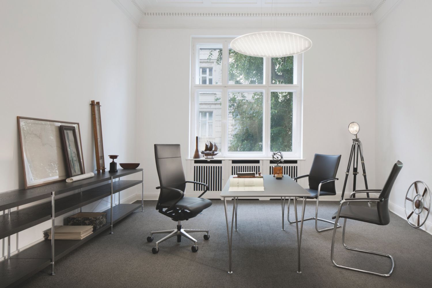 Modernes Büro mit ergonomischen Stühlen, Tisch, Regal und großem Fenster, das Tageslicht hereinlässt.