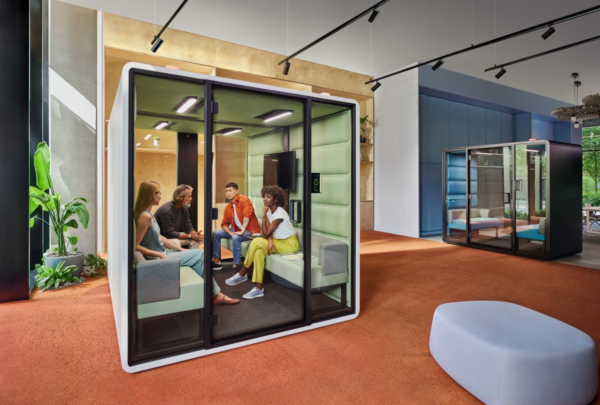 Gruppe von Menschen in einer modernen, schallisolierten Meeting-Box in einem gut beleuchteten Büro.