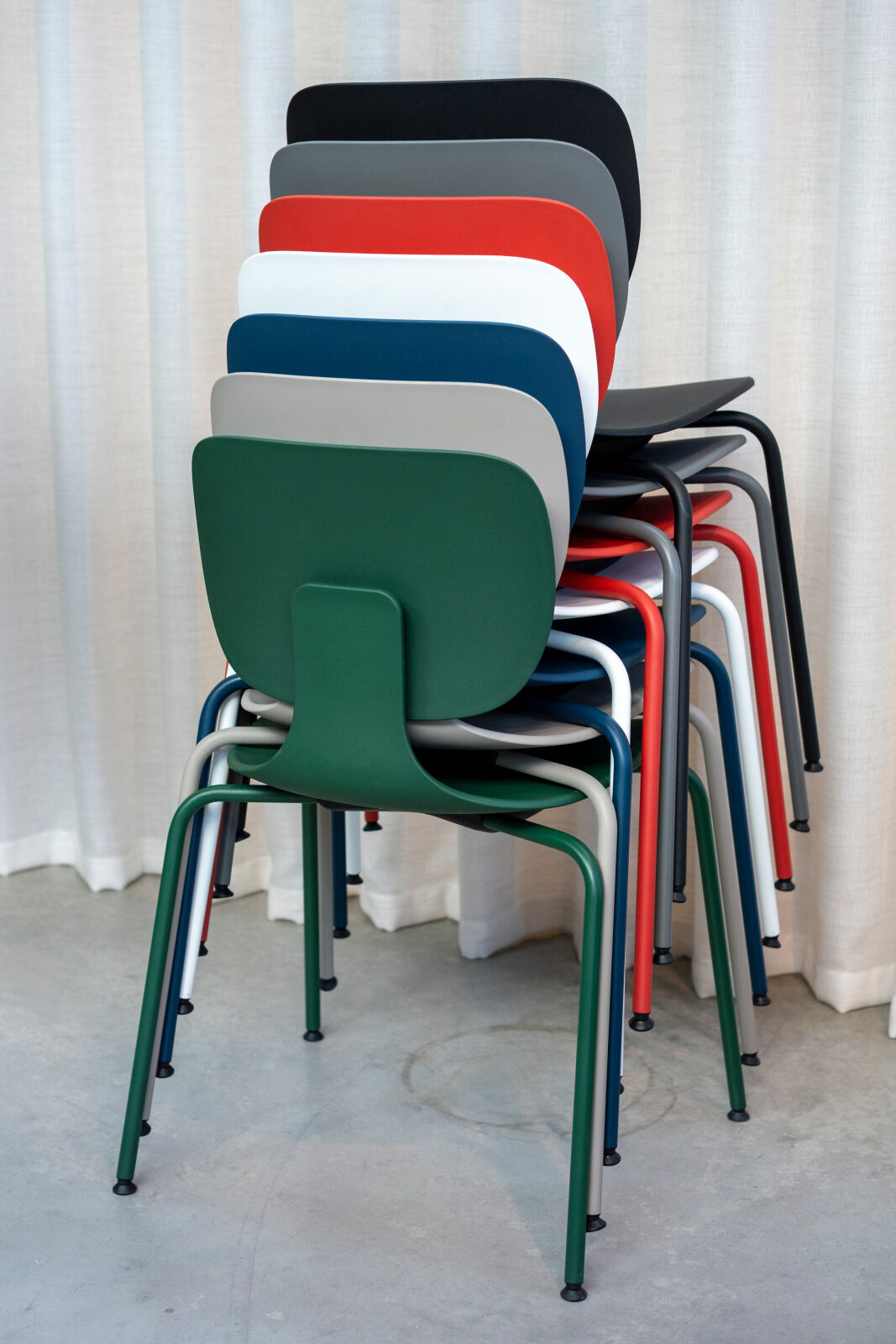 Stapel bunter ergonomischer Stühle vor einem weißen Vorhang, bestehend aus acht verschiedenen Farben.