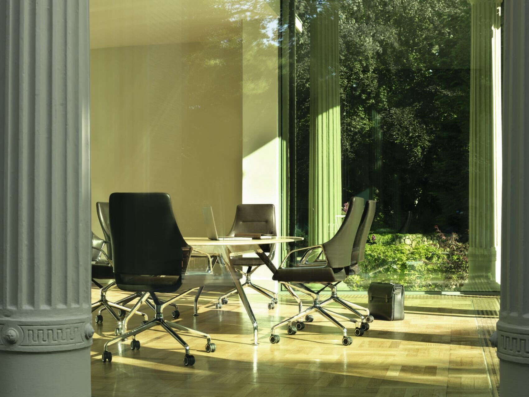 Ergonomische Bürostühle um einen Tisch in einem sonnigen Raum mit Blick auf einen grünen Garten.