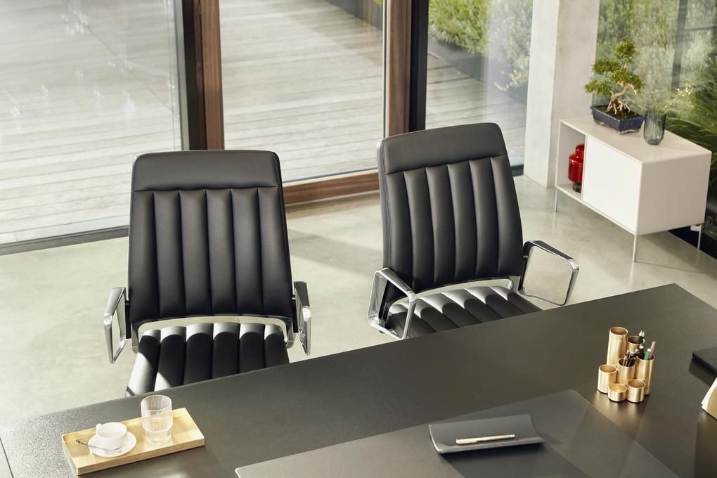 Zwei schwarze, ergonomische Bürostühle vor einem modernen Schreibtisch in einem hellen, stilvollen Büro.