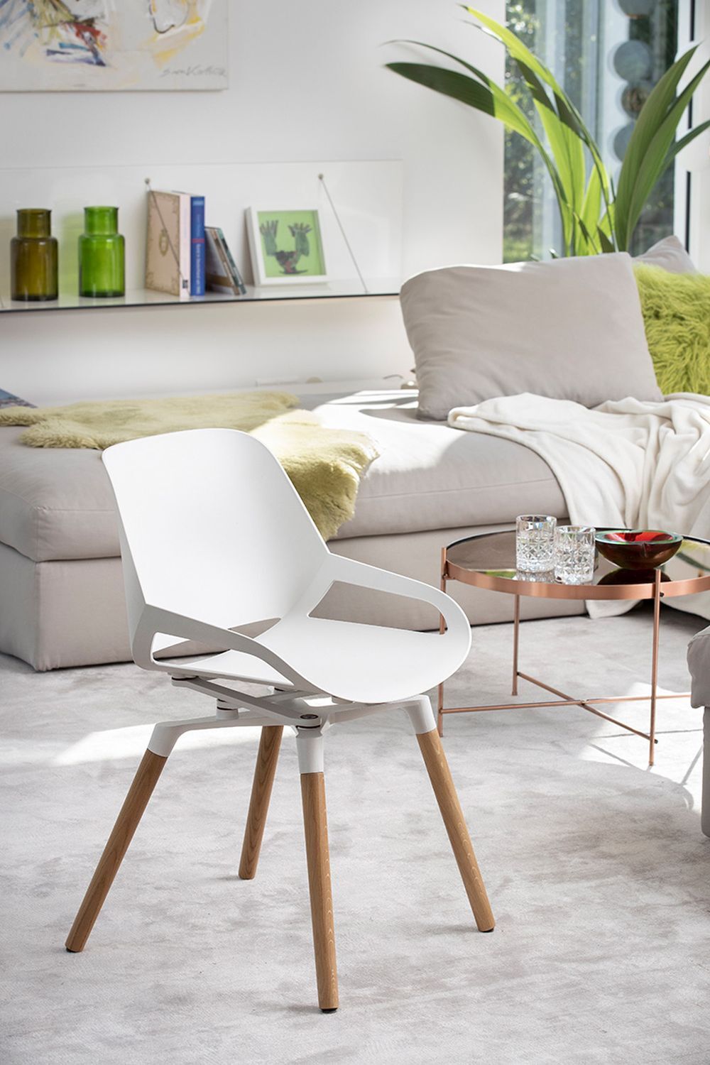 Moderner weißer Stuhl mit Holzbeinen in einem hellen Wohnzimmer, umgeben von Pflanzen und Bücherregalen.