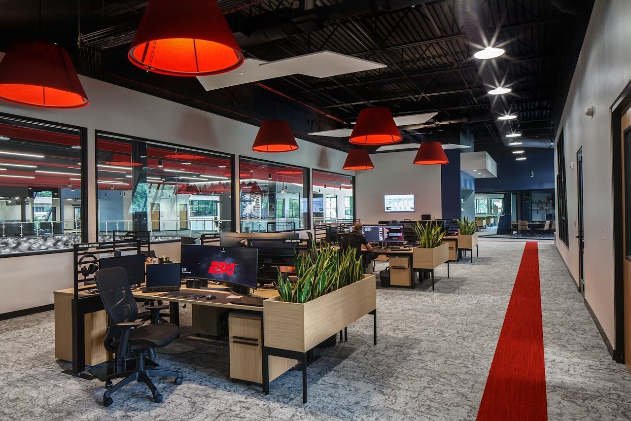 Modernes Büro mit ergonomischen Stühlen, großen Bildschirmen und roten Lampenschirmen für dynamisches Arbeiten.