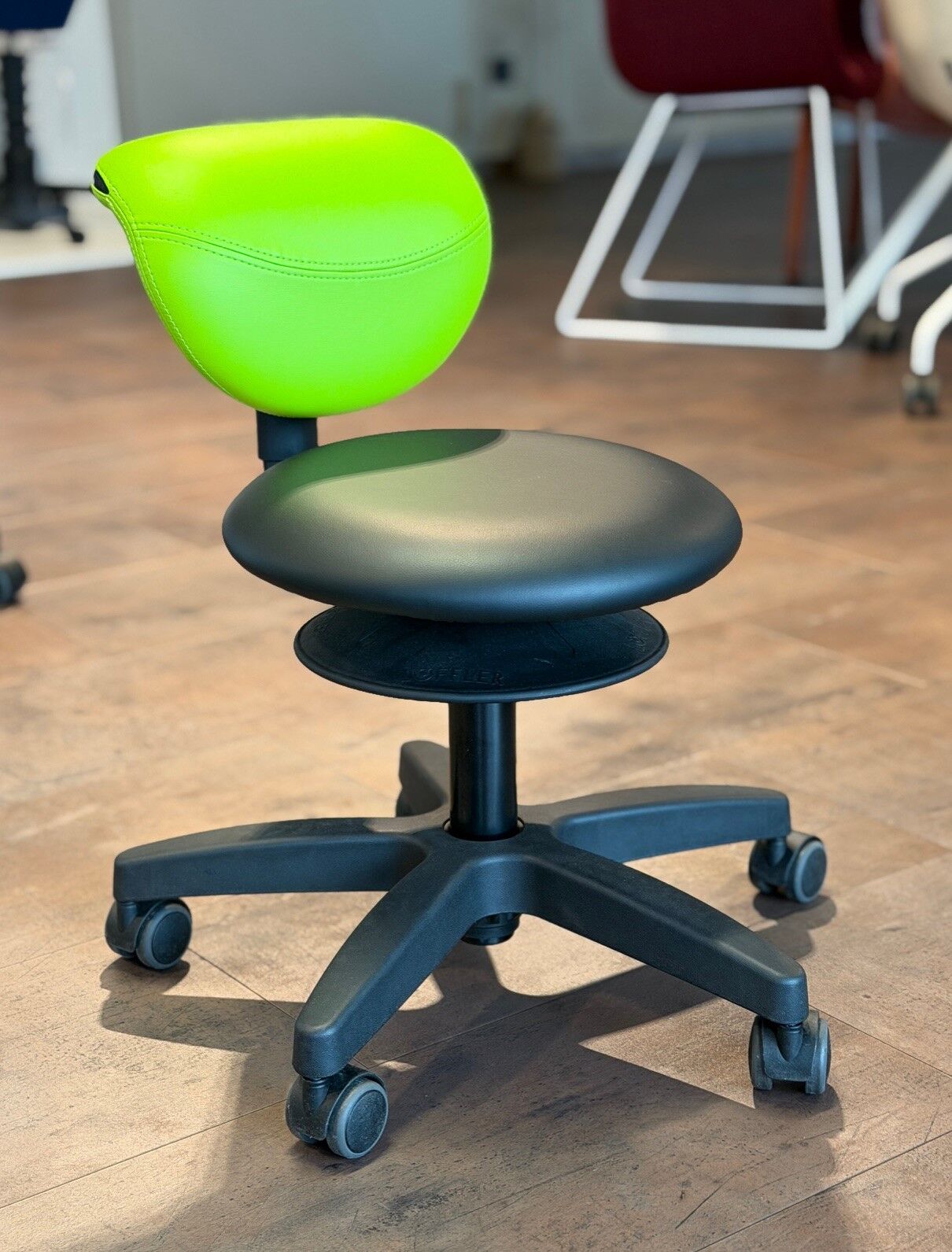 Moderner ergonomischer Bürostuhl mit grünem Rücken und schwarzem Sitz auf Holzfußboden in einem Ausstellungsraum.