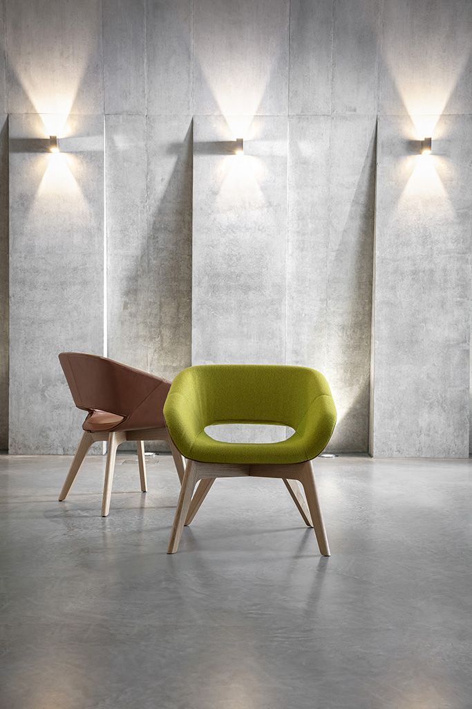 Zwei moderne Sessel vor Betonwand; einer grün, der andere braun, mit Holzbeinen und elegantem Design.