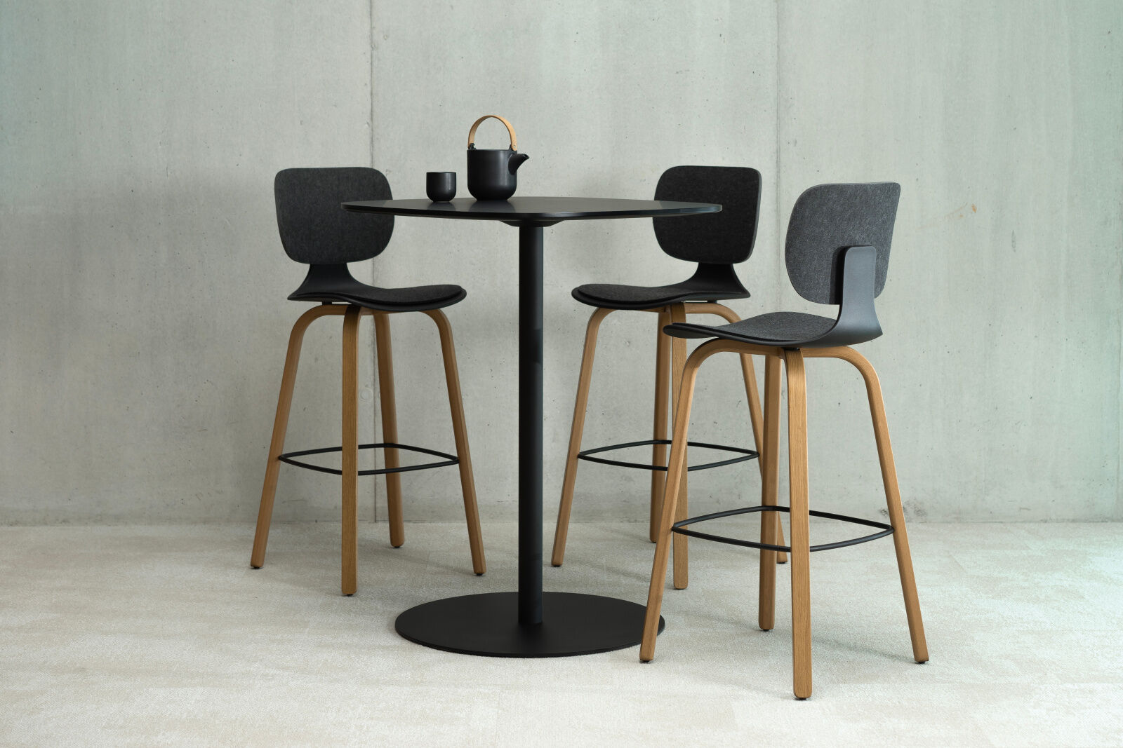 Drei moderne Barhocker mit Holzbeinen und schwarzer Polsterung, um einen schwarzen runden Tisch mit Teekanne.