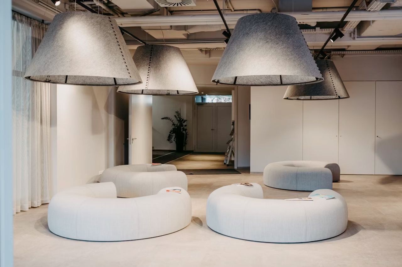 Moderne Lounge mit kreisförmigen Sofas und großen, trichterförmigen Deckenleuchten in einem minimalistischen Raum.