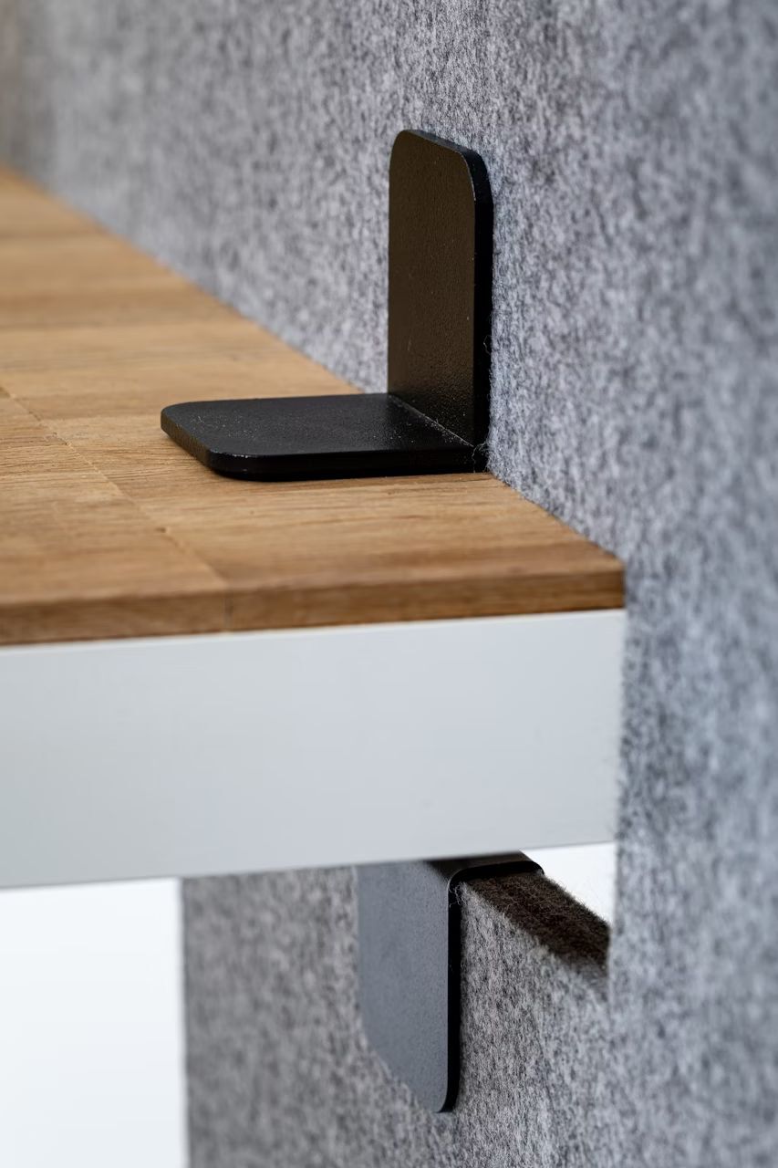 Nahaufnahme einer schwarzen Metallhalterung, die einen Holztisch mit einer Filztrennwand verbindet.
