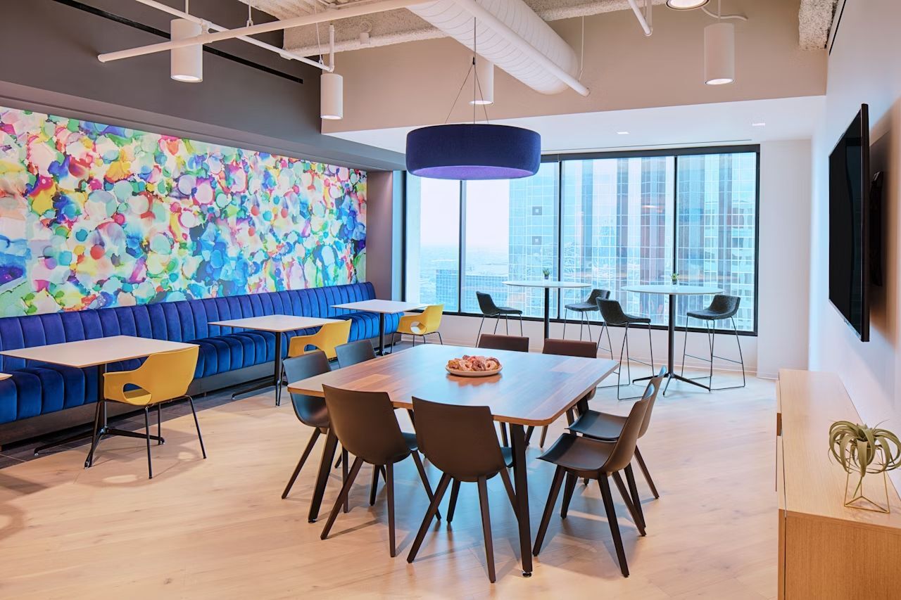 Moderner Büroraum mit buntem Wandbild, ergonomischen Stühlen und großen Fenstern mit Stadtblick.