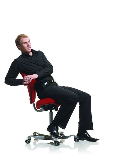 Mann lehnt sich entspannt auf einem ergonomischen Bürostuhl mit rotem Sitz.