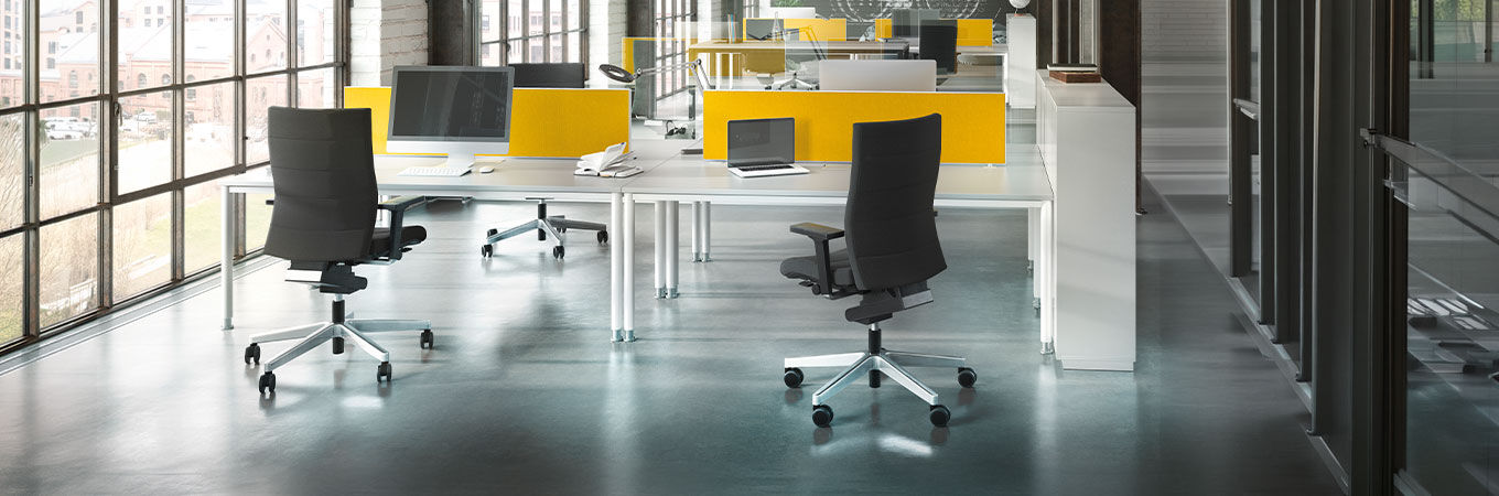 Moderne Büroumgebung mit ergonomischen Stühlen und Schreibtischen, betont durch gelbe Trennwände und große Fenster.
