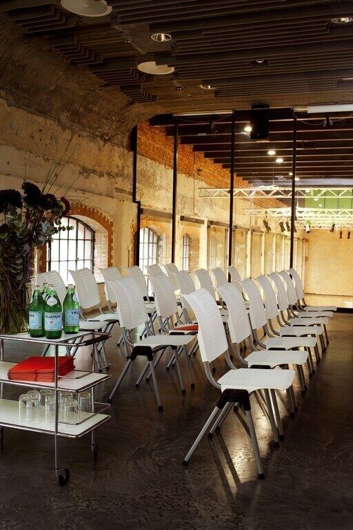 Moderner Konferenzraum mit weißen Stühlen in Reihen, neben einem Tisch mit Wasserflaschen und Gläsern.