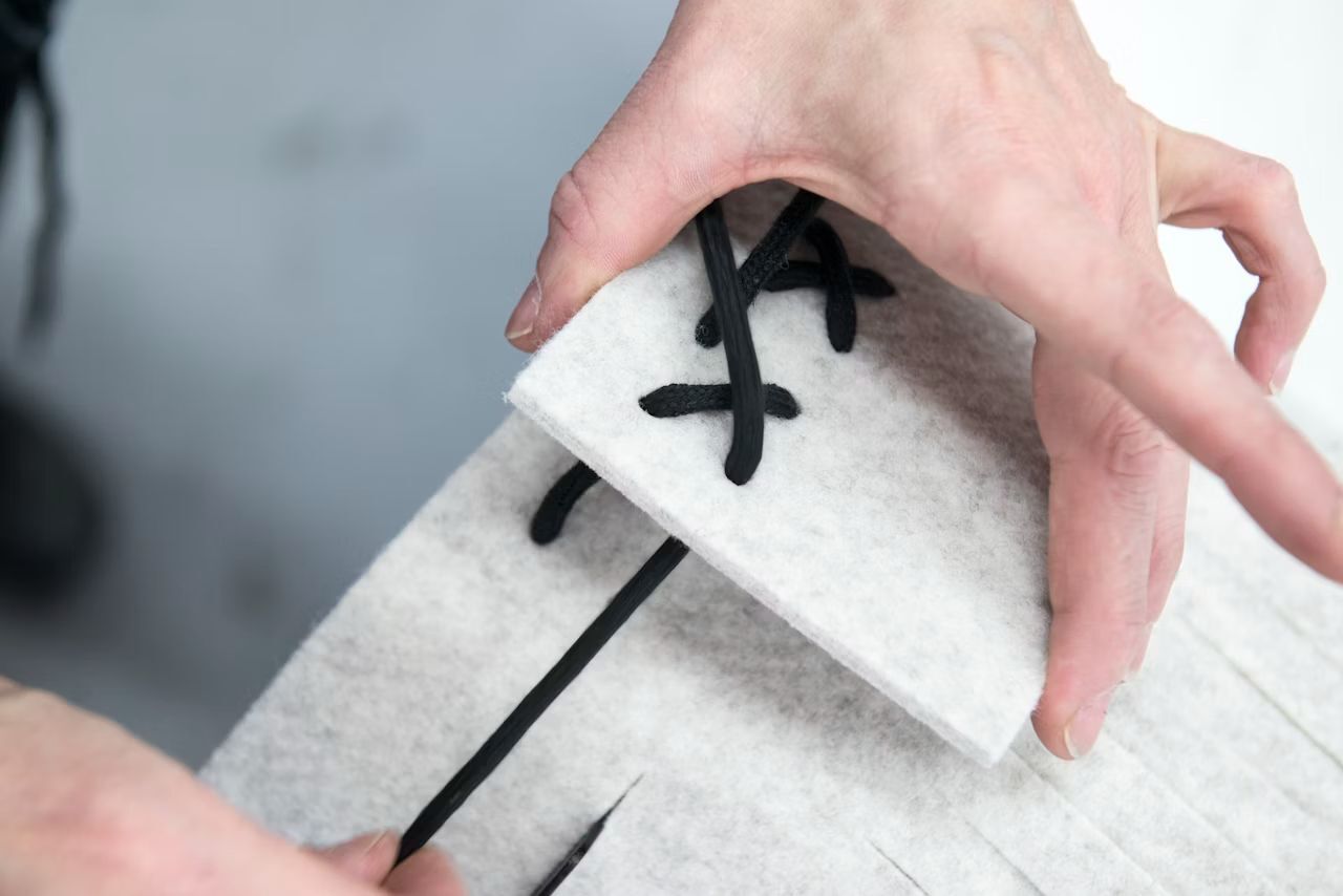 Nahaufnahme einer Person, die ein schwarzes Band durch weißen Filz für ergonomische Möbel zieht.