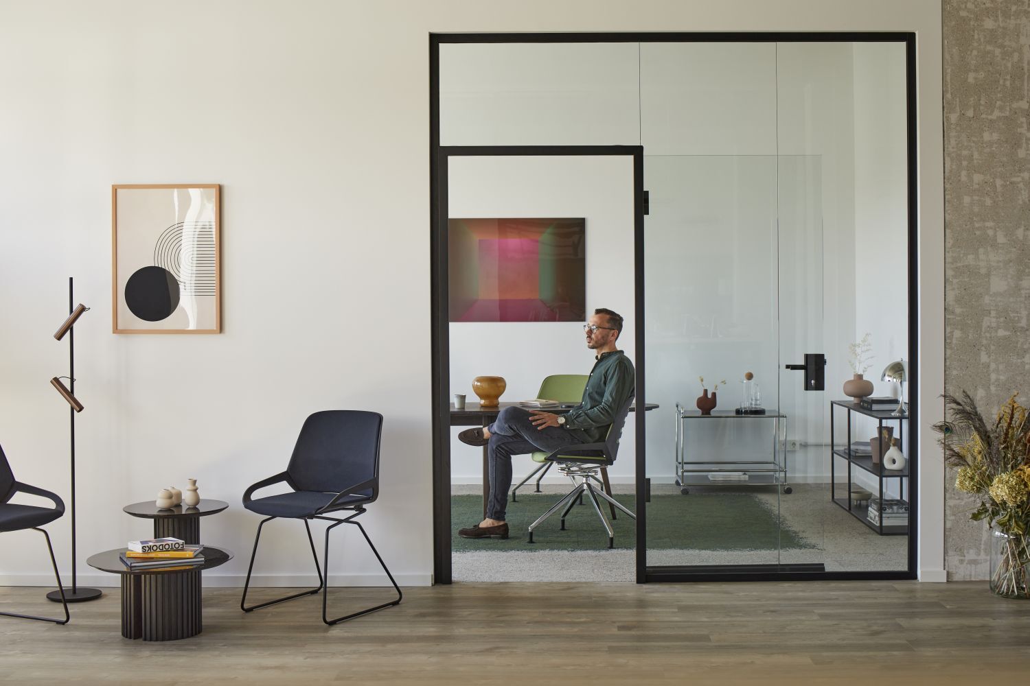 Mann sitzt in einem modernen, ergonomischen Bürostuhl in einem stilvollen Büro mit Glaswänden.
