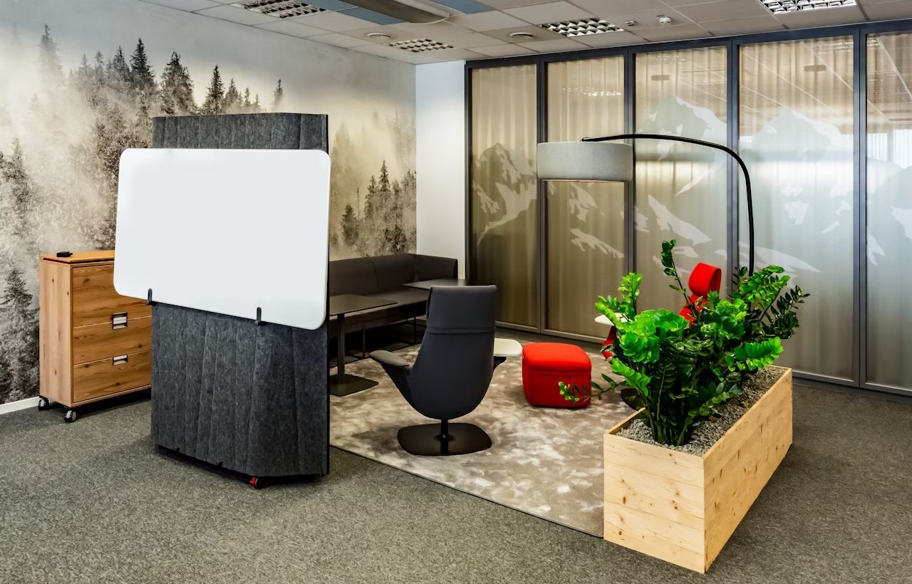 Modernes Büro mit ergonomischen Stühlen, Tisch, Pflanzen und Trennwand vor einer Waldtapete.