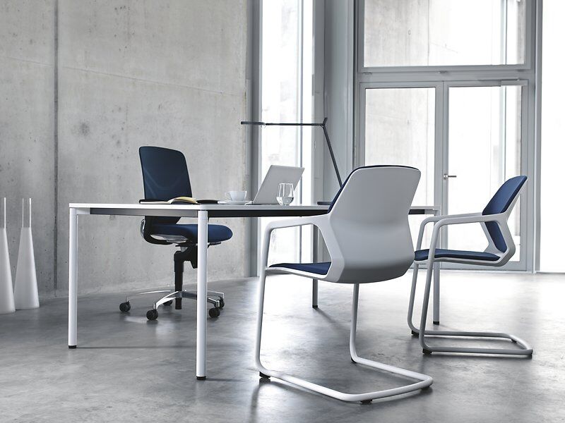 Ergonomischer Bürostuhl und Tisch in moderner Büroumgebung mit Betonwänden und Glasfenstern.
