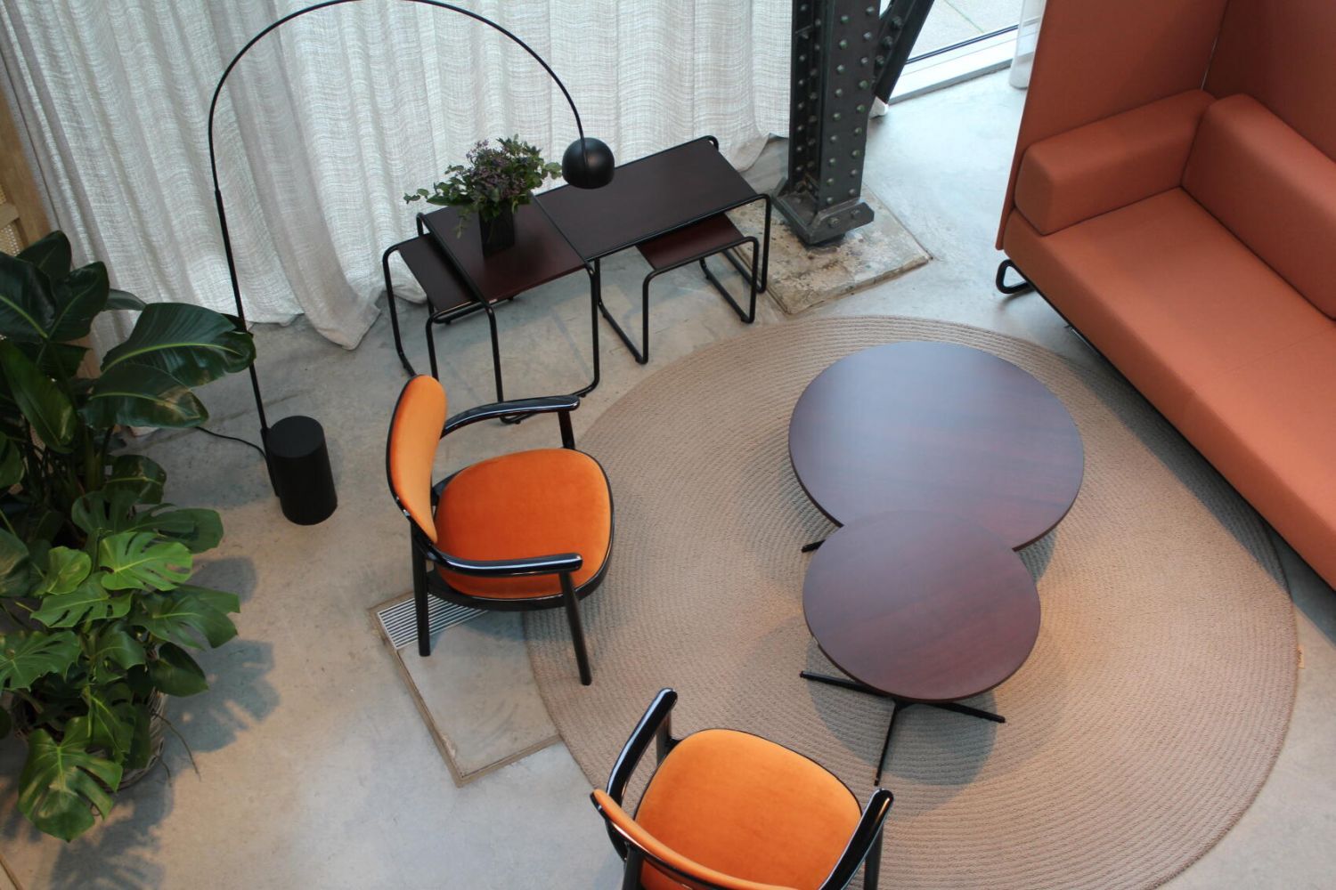 Moderner Lounge-Bereich mit orangefarbenen Sesseln, runden Tischen, Pflanzen und dekorativen Akzenten.