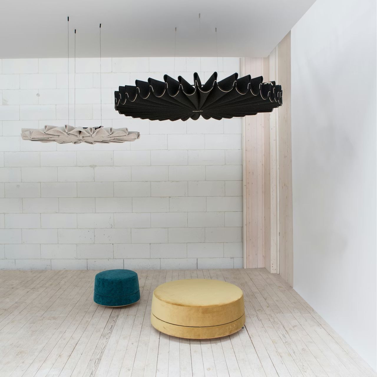 Moderne Raumgestaltung mit schwarzem und weißem Akustik-Pendelleuchten, samtigem Hocker und Pouf auf Holzboden.