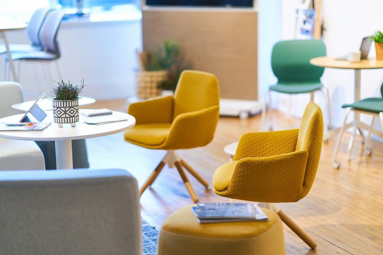 Helle Büroeinrichtung mit gelben ergonomischen Stühlen, weißen Tischen und grünen Pflanzen für ein dynamisches Sitzen.