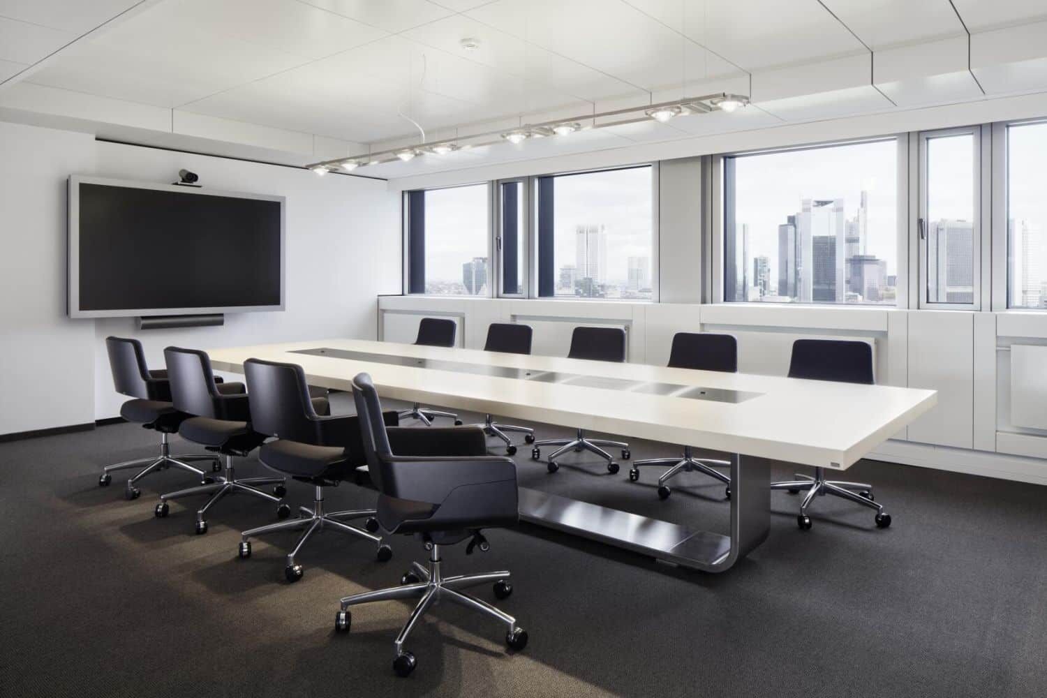 Moderner Konferenzraum mit ergonomischen Bürostühlen und großem Tisch, Blick auf die Stadt im Hintergrund.