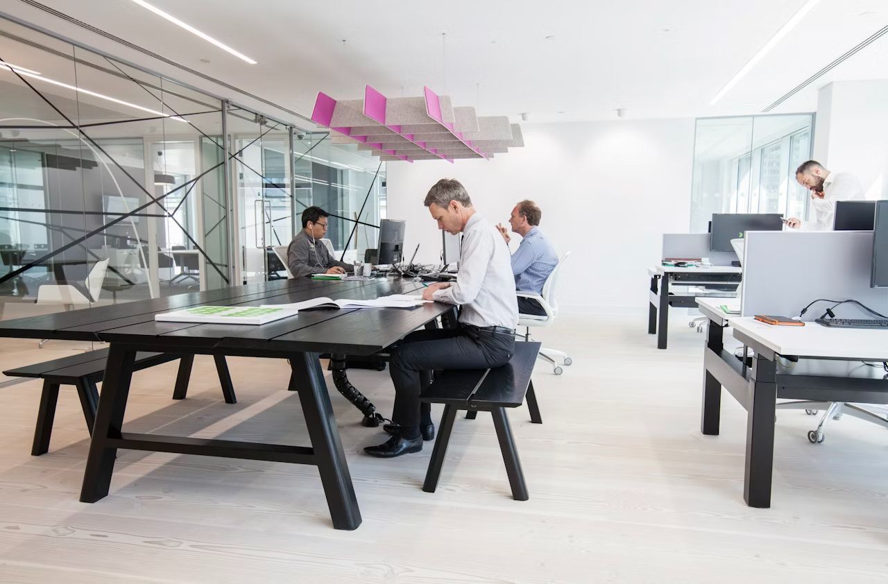 Offenes Büro mit vier Männern an ergonomischen Schreibtischen, konzentriert bei der Arbeit in einem modernen Raum.