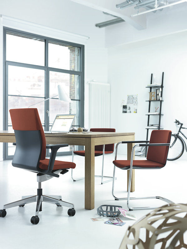 Moderner Büroarbeitsplatz mit ergonomischen Stühlen, Holztisch, Laptop und Fahrrad im Hintergrund, hell beleuchtet.