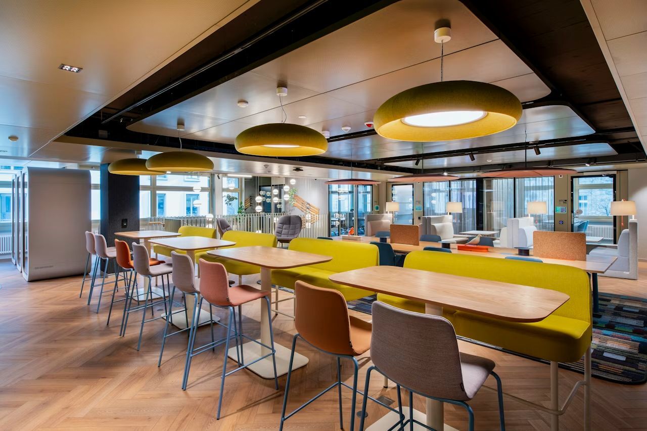 Moderne Büroumgebung mit ergonomischen Stühlen, langen Holztischen und stilvollen Hängelampen, ideal für Teamarbeit.