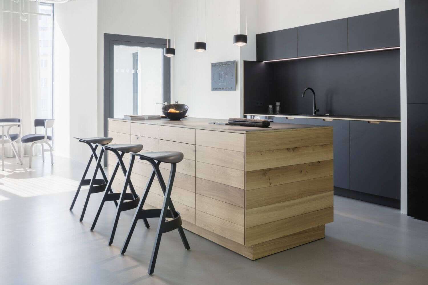 Moderne Küche mit Holzinsel, schwarzen Hockern, grauen Schränken und heller Einrichtung.