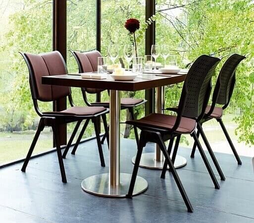 Moderner Esstisch mit vier ergonomischen Stühlen, gedeckt mit Gläsern, in einem lichtdurchfluteten Raum mit Blick ins Grüne.