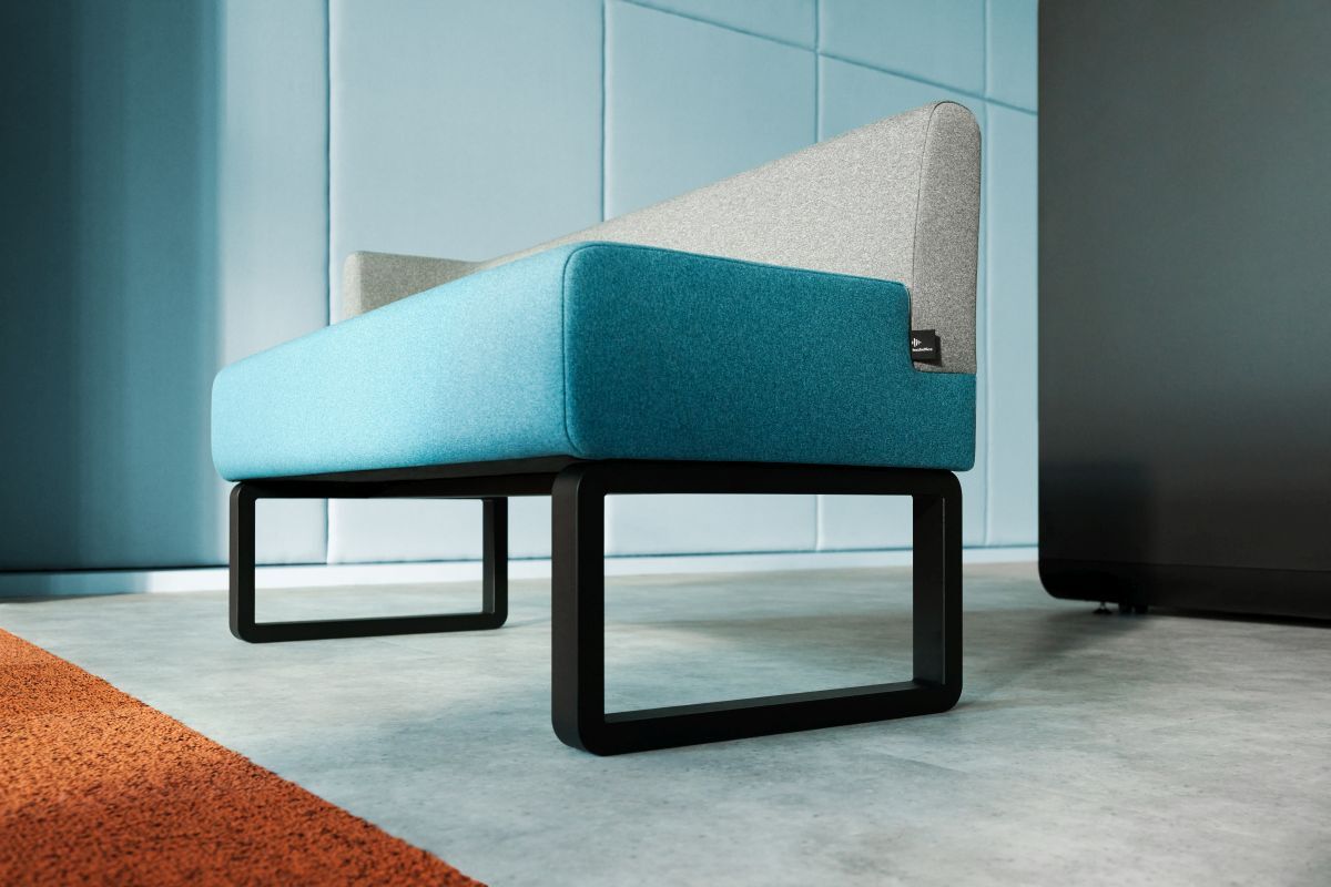 Moderne Couch mit blauer und grauer Polsterung, schwarzem Metallgestell, auf Betonboden vor blauer Wand.