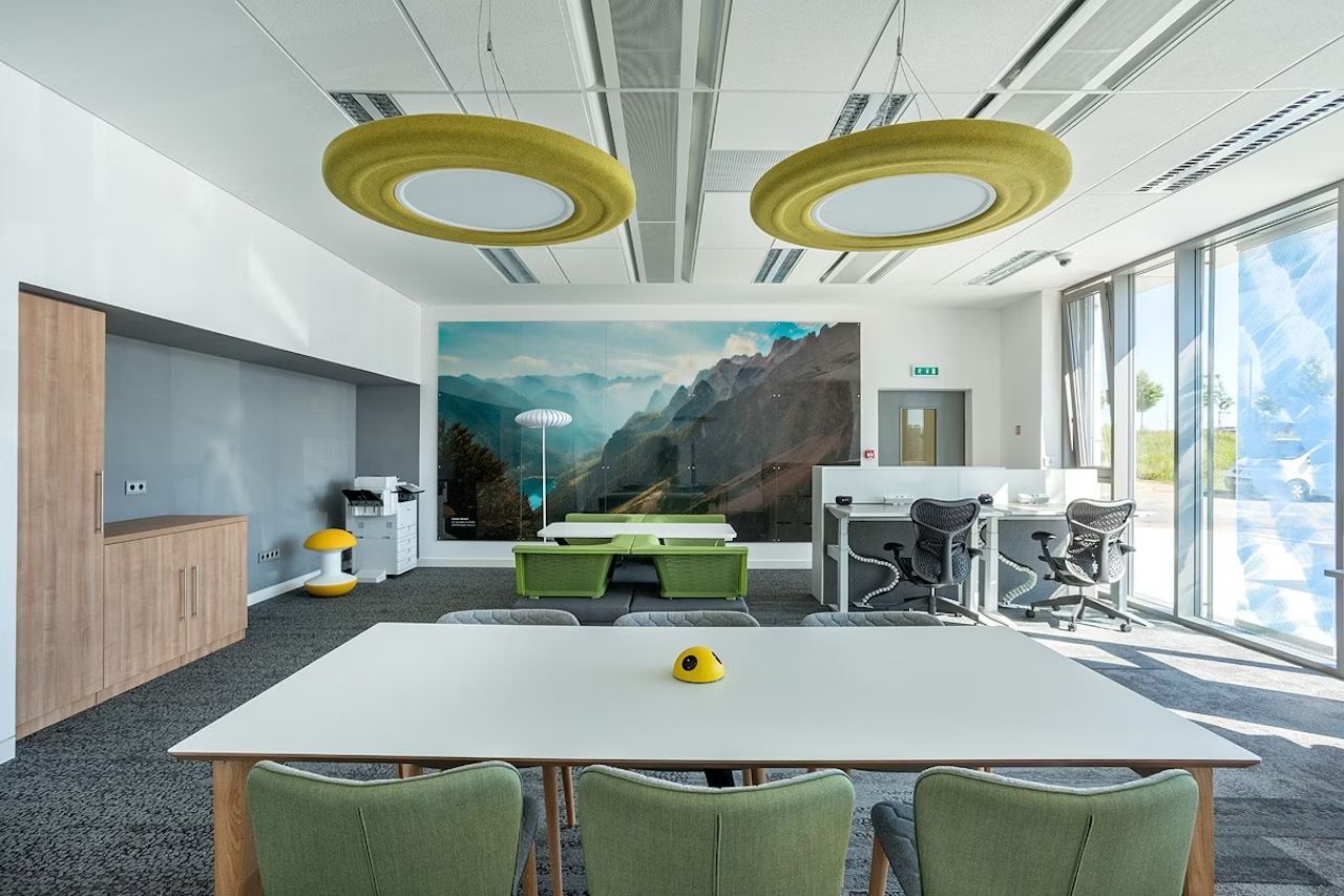 Moderner Büroraum mit ergonomischen Bürostühlen, einem großen Tisch und einer Berglandschaft an der Wand.