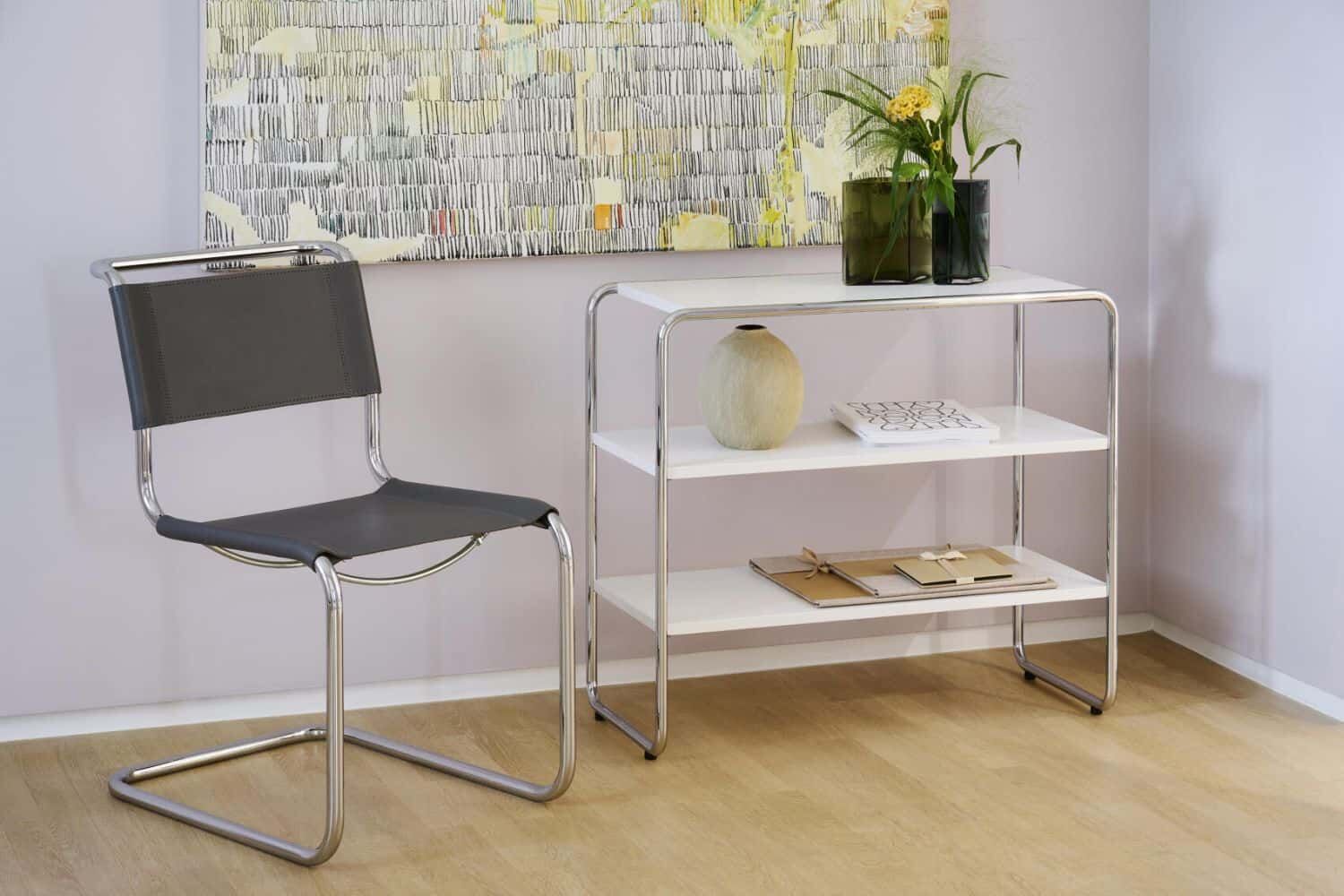 Moderner Stuhl mit Metallrahmen neben einem Regal, dekoriert mit Pflanzen und Kunstwerken, auf Holzboden.
