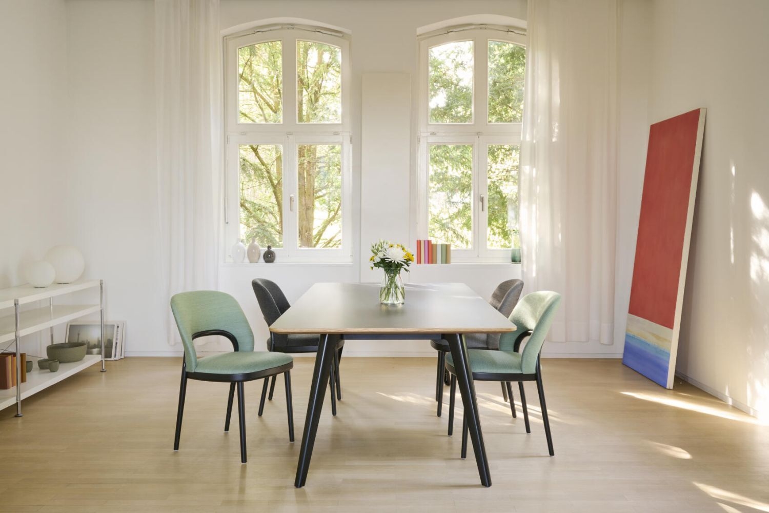 Moderner Besprechungsraum mit Tisch, farbigen Stühlen und großer Fensterfront, die viel natürliches Licht hereinlässt.