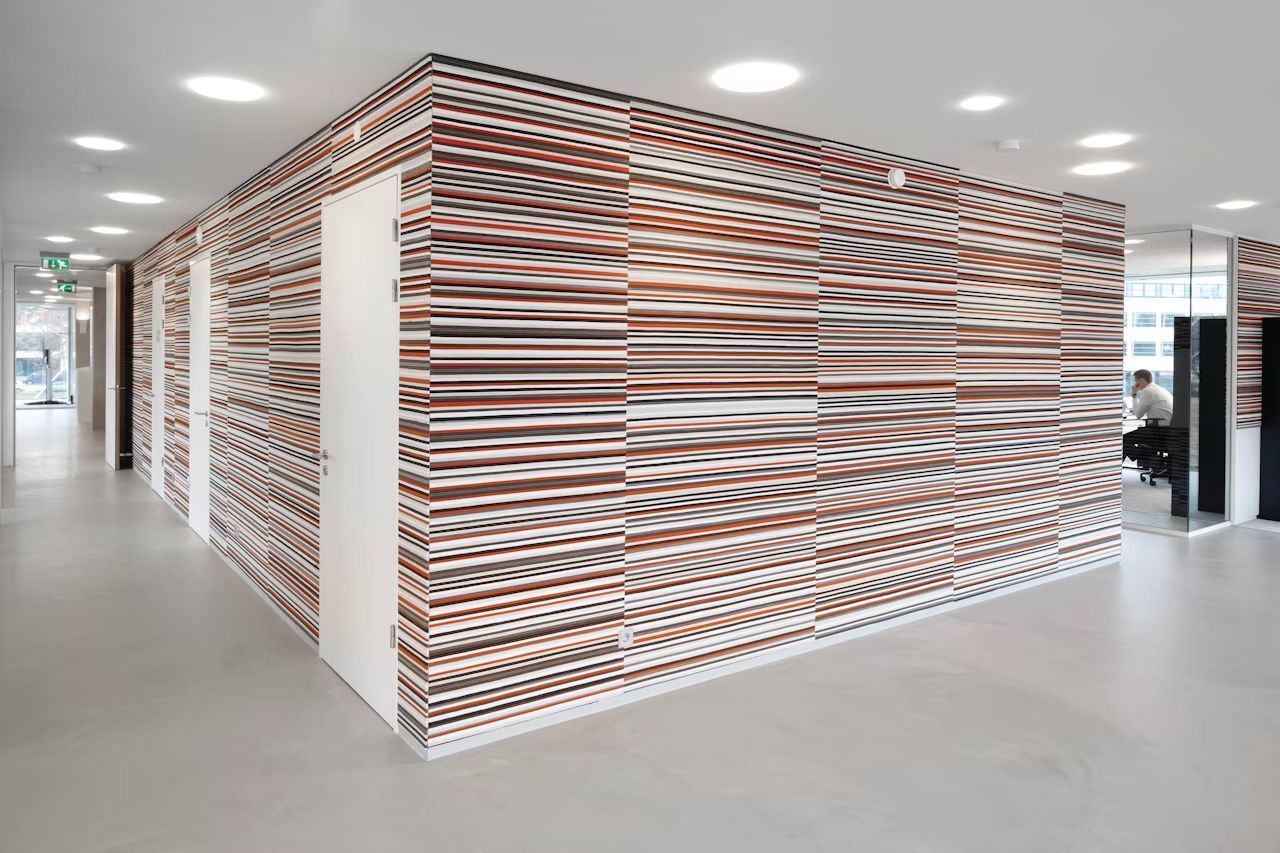 Modernes Büro mit gestreiften Wänden und Glasabteilen fördert ergonomisches Arbeiten in kreativer Umgebung.