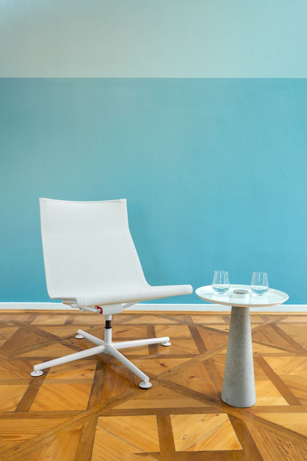 Ergonomischer weißer Stuhl neben einem minimalistischen Tisch mit zwei Gläsern vor einer blauen Wand.