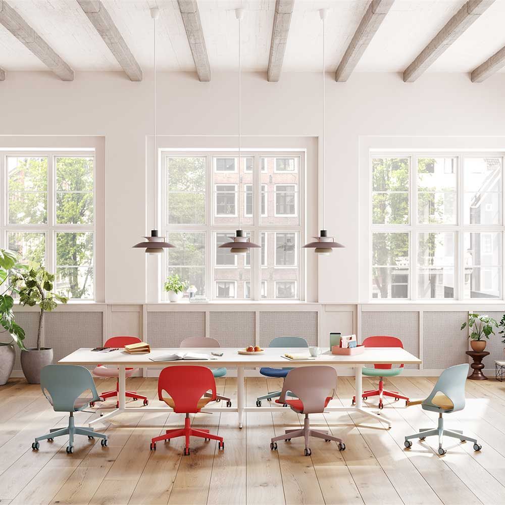 Moderne Büroumgebung mit bunten ergonomischen Stühlen und einem großen Besprechungstisch, beleuchtet durch große Fenster.