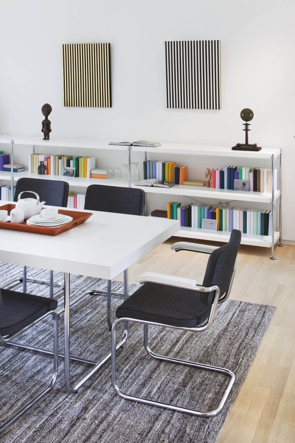 Moderner Konferenzraum mit schwarzen Freischwingerstühlen, weißem Tisch und Bücherregalen an einer weißen Wand.