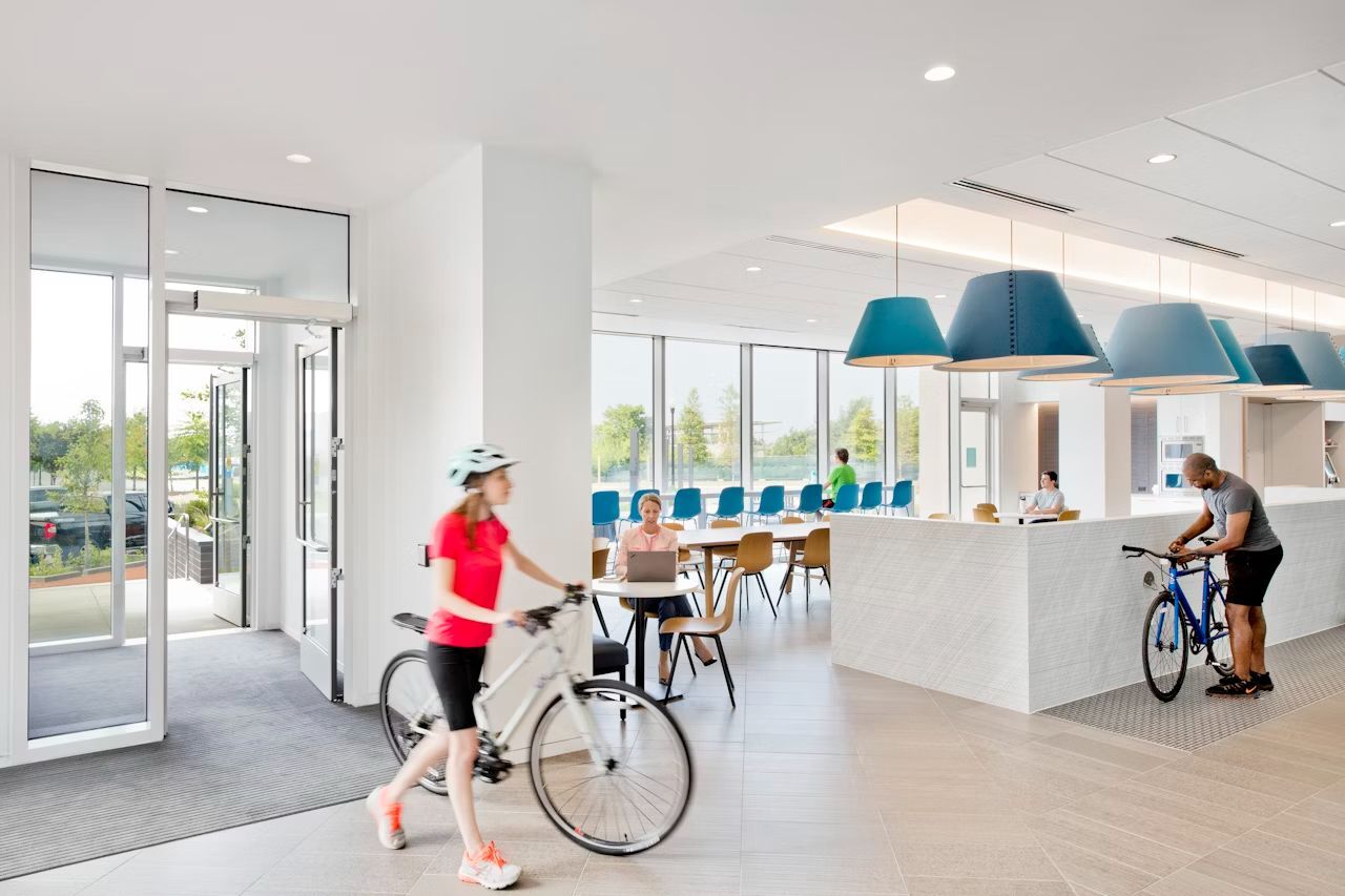 Menschen in einem modernen Büro, eine Frau mit Fahrrad, Angestellte arbeiten an Laptops. Helle, offene Gestaltung.