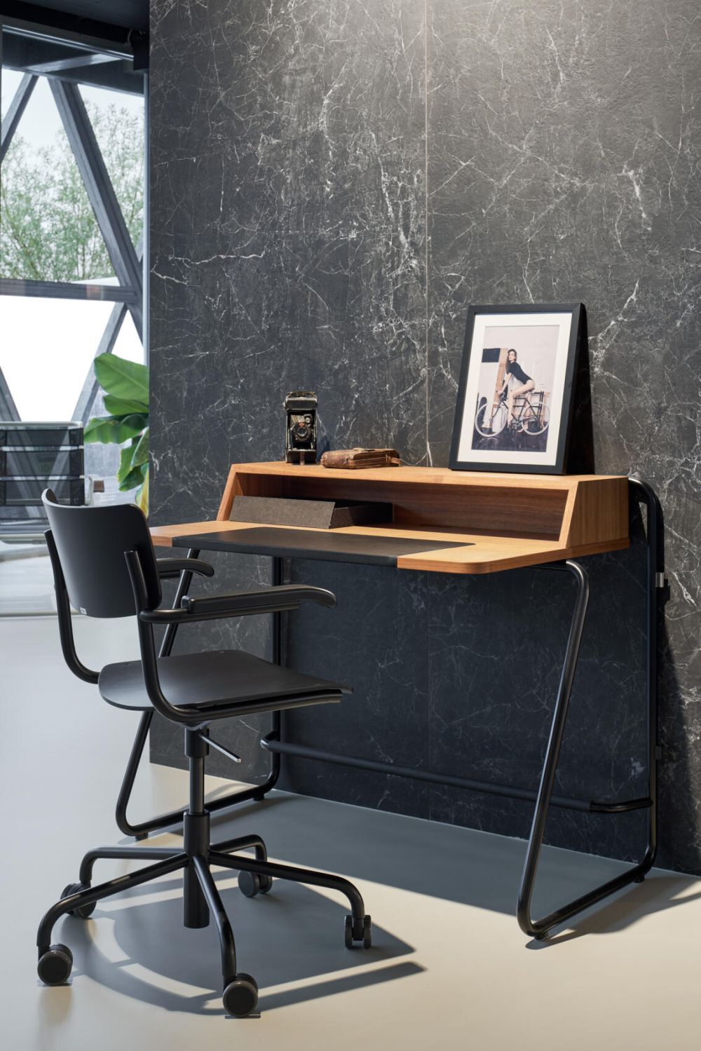 Moderner ergonomischer Bürostuhl vor Holztisch mit Dekoration und gerahmtem Foto, auf grauem Marmorboden.