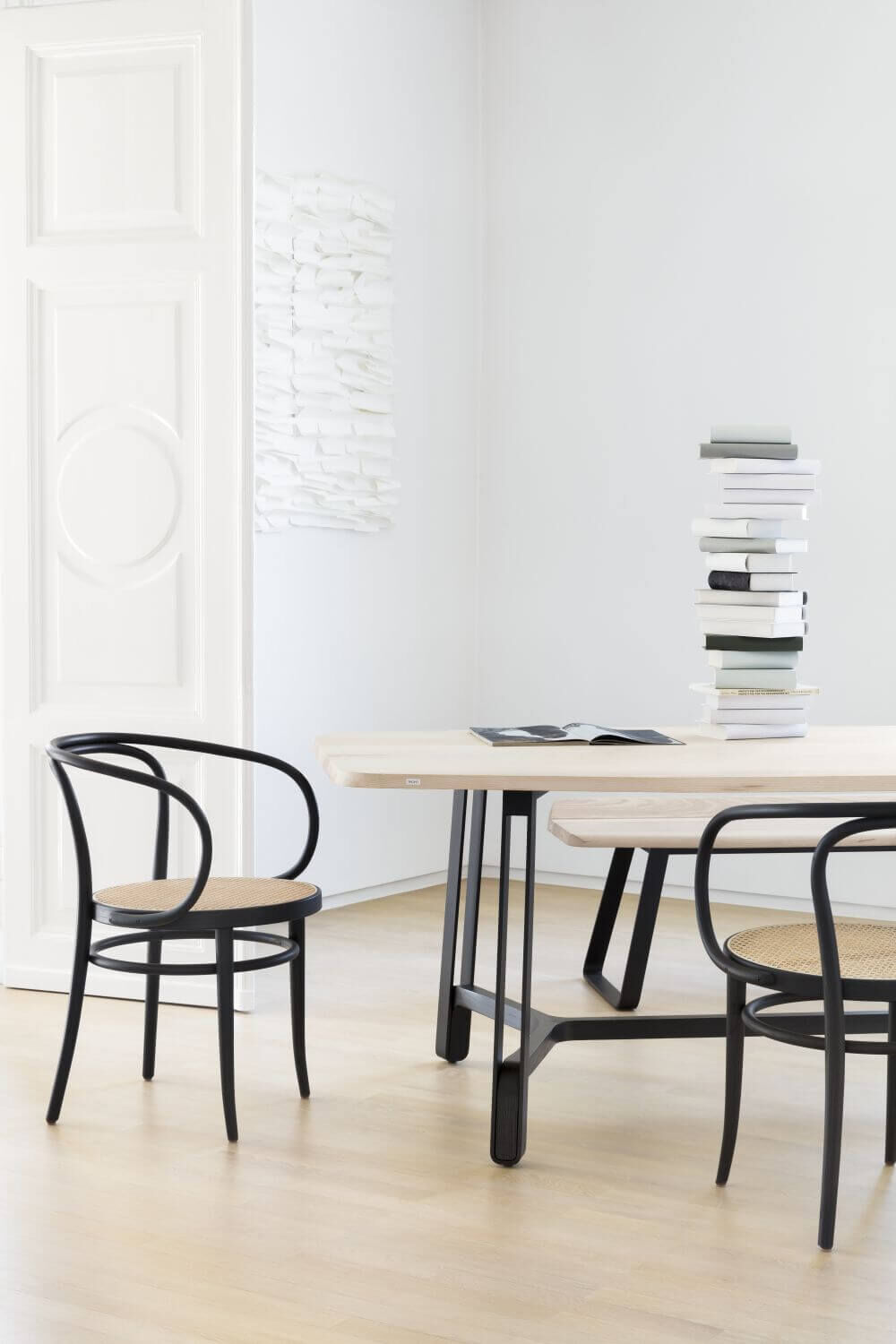 Minimalistischer Raum mit Holzstuhl, Tisch und Bücherstapel, betont schlichtes, elegantes Design.