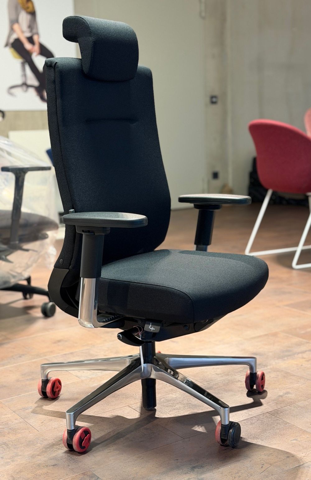Schwarzer ergonomischer Bürostuhl mit Kopfstütze und roten Rollen, ideal für gesundes, dynamisches Sitzen im Büro.